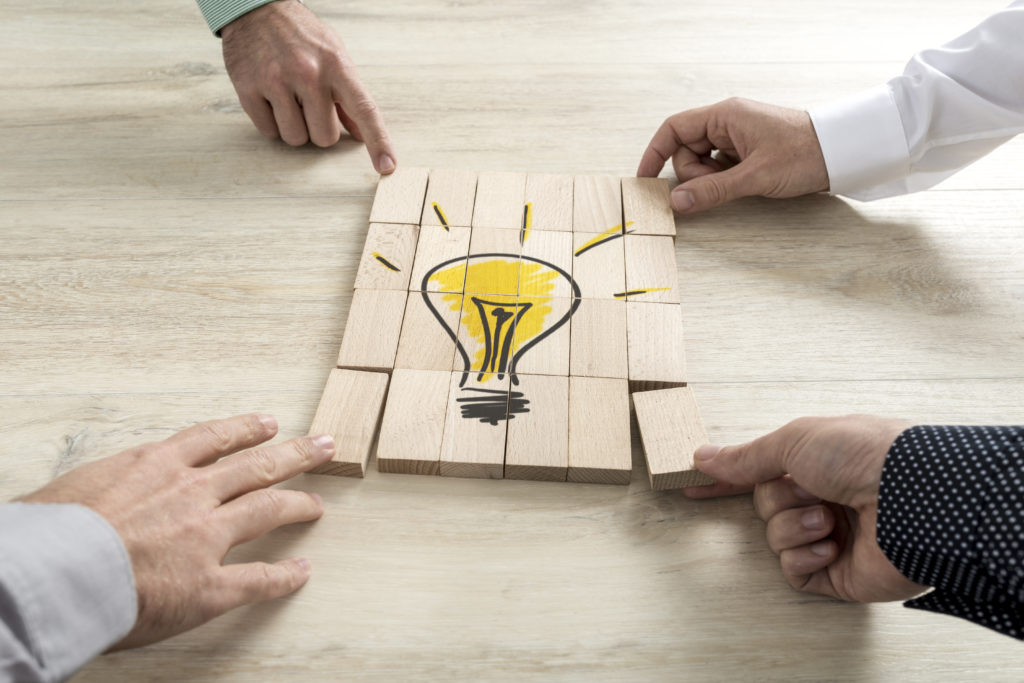 Four businessmen holding pieces of a wooden bricks bearing the image of a light bulb conceptual of business strategy, creativity or teamwork.