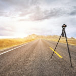 Professional photo camera on tripod on an empty road at sunset, focus on the camera, travel or work concept, Badlands National Park, South Dakota, USA.